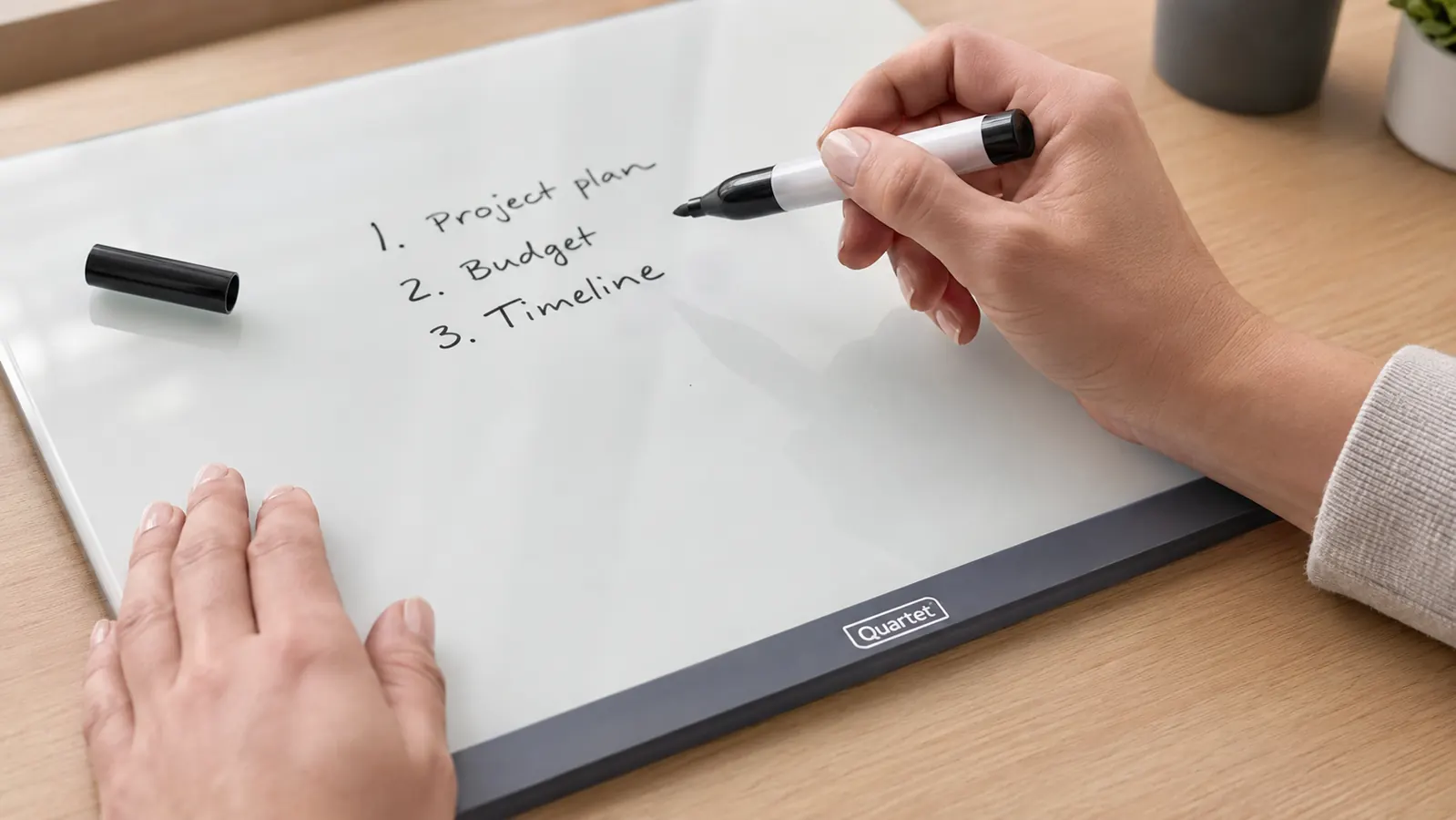 Hand writing the day's top three tasks on a glass whiteboard with a dry erase marker