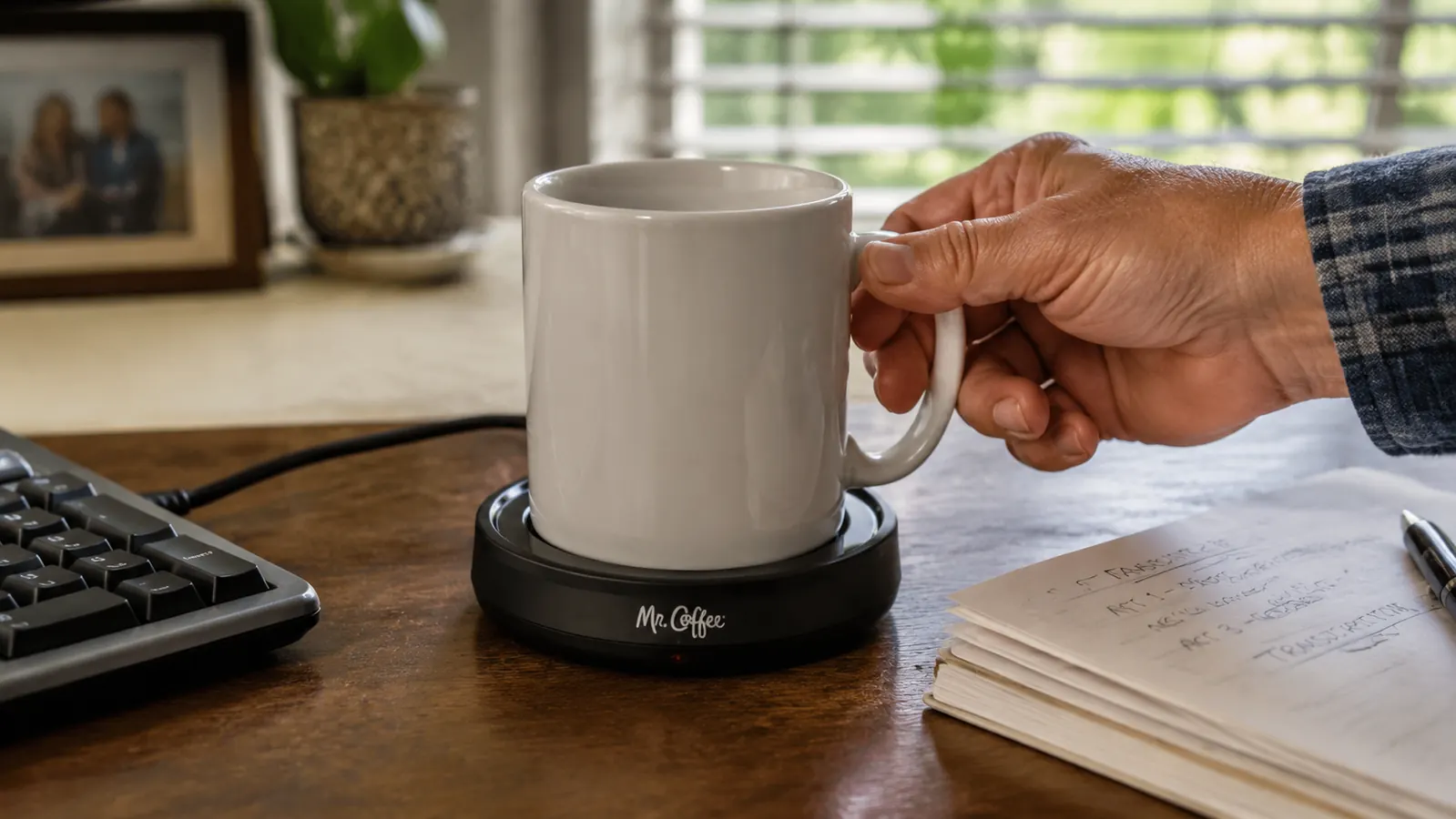Hand setting a flat-bottomed ceramic mug onto the Mr. Coffee mug warmer plate at a desk